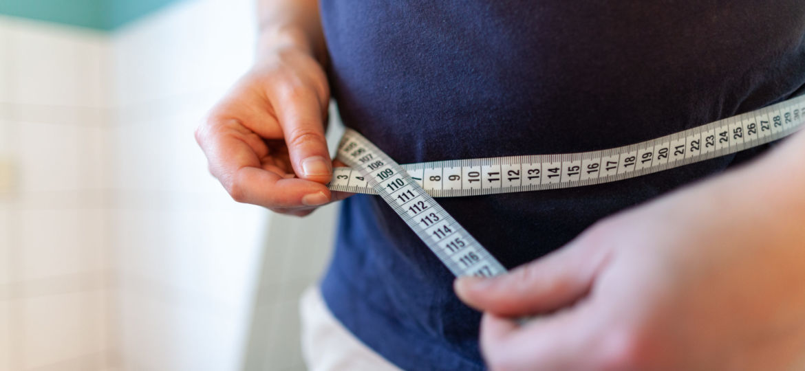 man measures her abdomen with a measuring tape
